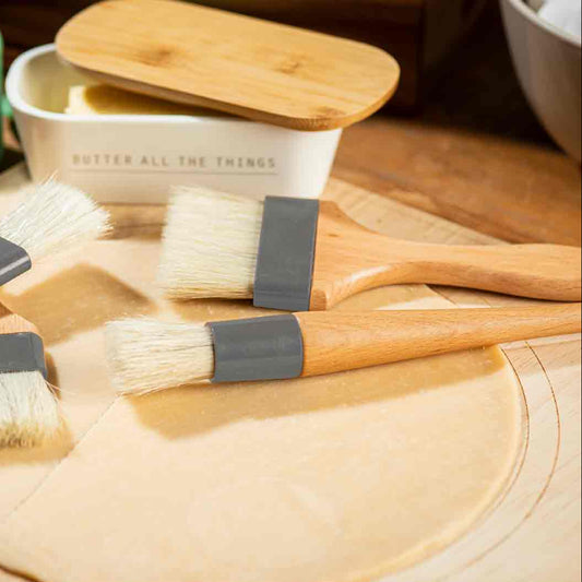 Set of wooden cooking brushes with gray bristles on a wooden surface.