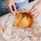 Person unwrapping a loaf of bread with patterned paper on a white surface