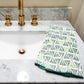 Bathroom sink with marble countertop and gold faucet, featuring a green patterned towel.