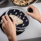 Person preparing food on a cutting board with a container of ingredients.