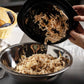 Shredded chicken being transferred from a black bowl to a metal bowl on a kitchen counter.