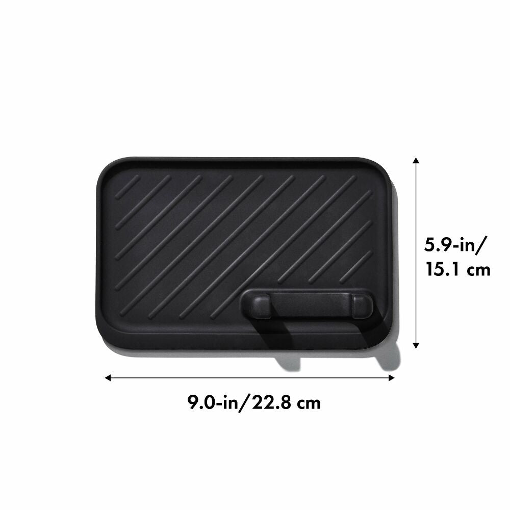 Black rectangular silicone trivet or heat deflector with diagonal ribbed texture and a small integrated handle, shown with dimension labels of 9.0-in/22.