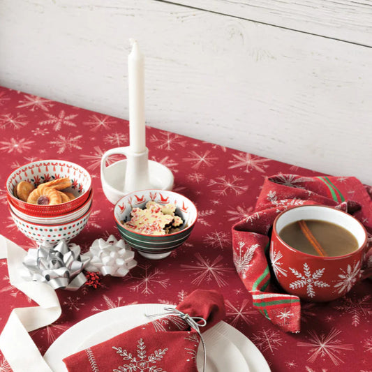 Christmas-themed table setting with red snowflake-patterned tablecloth, white plates, and festive decor.