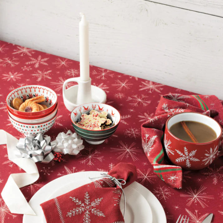 Christmas-themed table setting with red snowflake-patterned tablecloth, white plates, and festive decor.