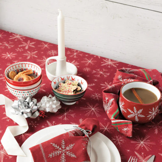 Christmas-themed table setting with red snowflake-patterned tablecloth, white plates, and festive decor.