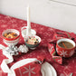 Christmas-themed table setting with red snowflake-patterned tablecloth, white plates, and festive decor.