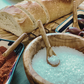 olive wood mini scoop spoon being used with salt and other spices on a table with bread