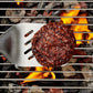 Hamburger patty being flipped on a grill with flames and coals visible