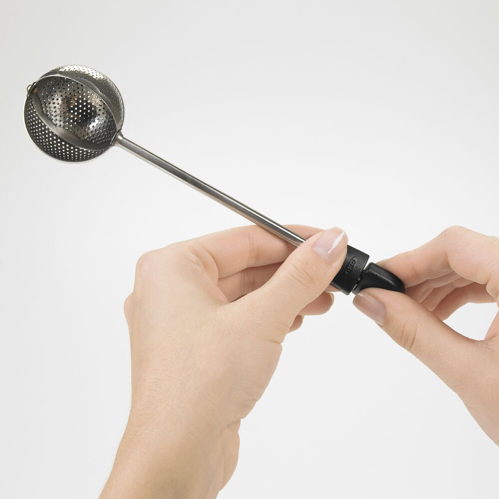 Metallic tea infuser held by a hand against a white background