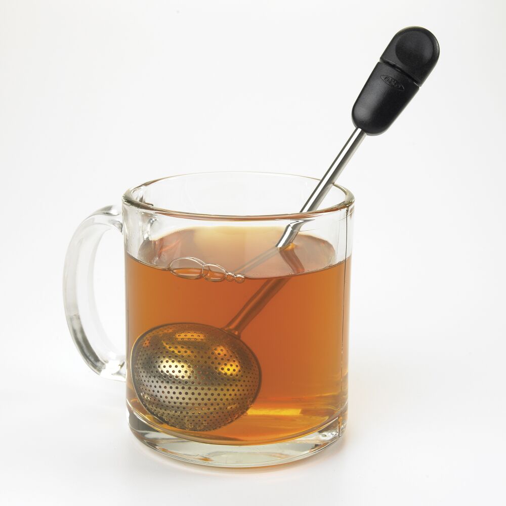 Glass mug with tea being brewed, featuring a metal tea ball and black handle on a white background