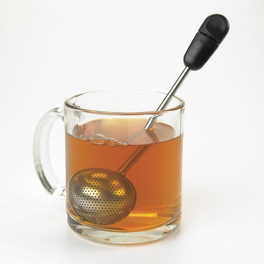 Glass mug with tea being brewed, featuring a metal tea ball and black handle on a white background