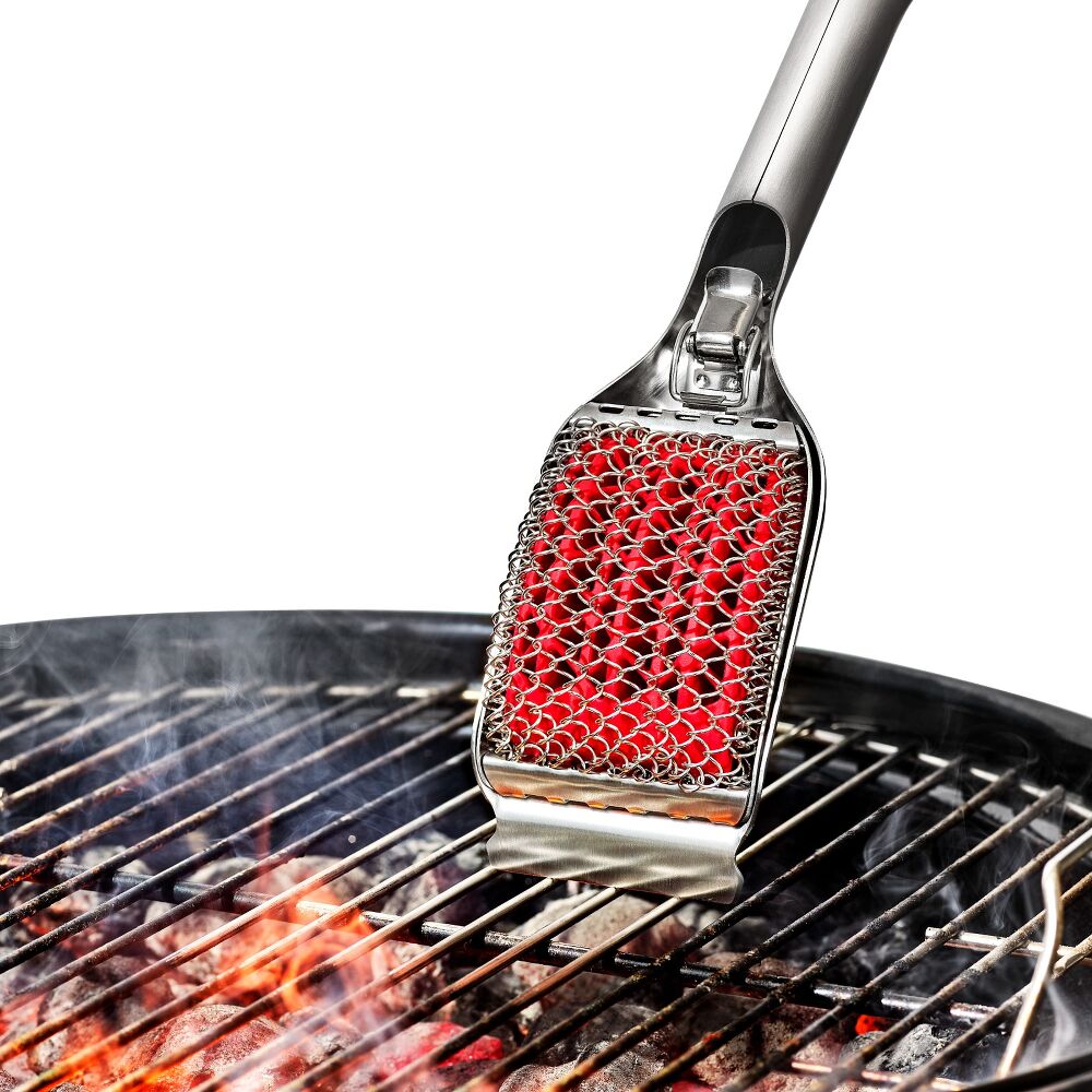 Metallic grill brush with red silicone head on a grill