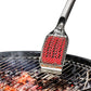 Metallic grill brush with red silicone head on a grill