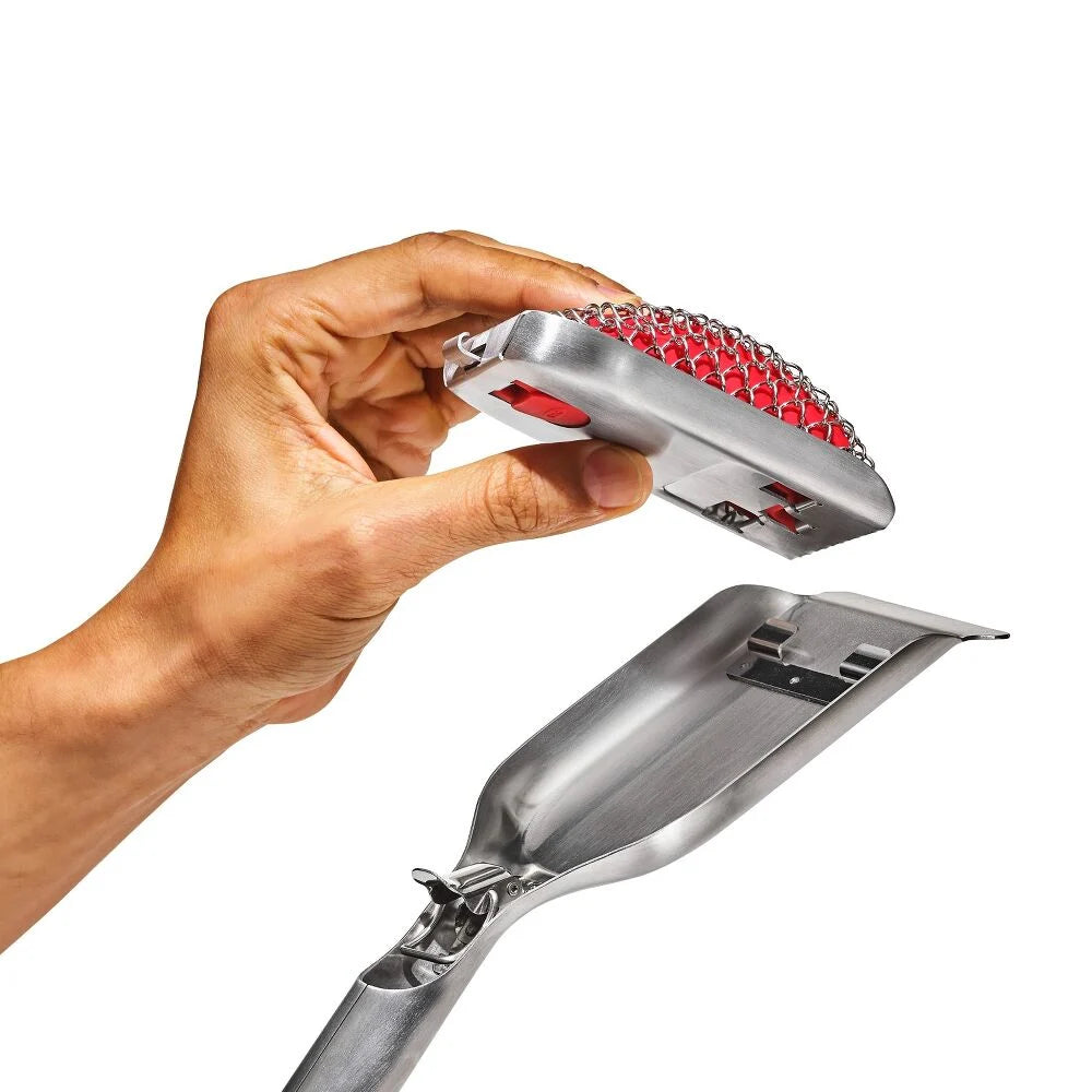 Hand holding a metal grill brush head with red bristles against a white background