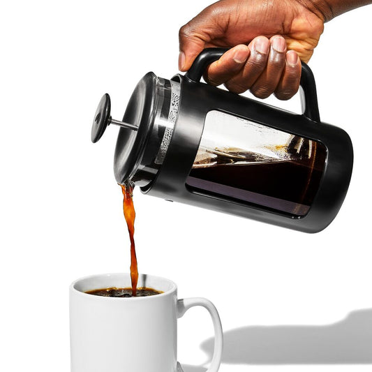 Hand pouring coffee from a French press into a white mug on a white background