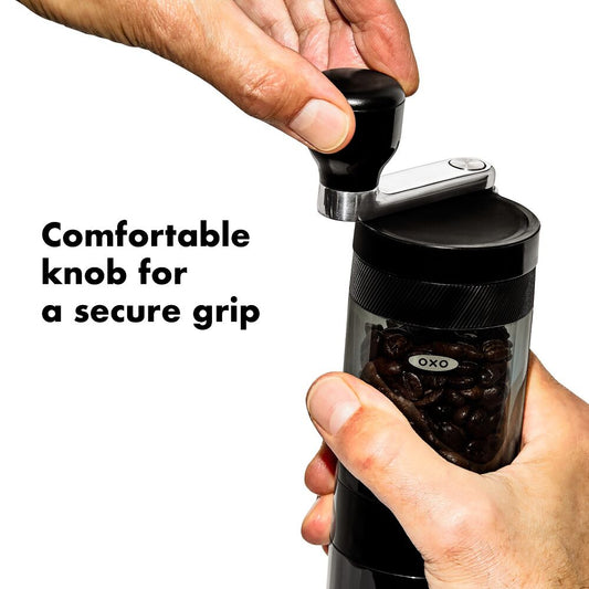 Hand holding a black OXO coffee grinder with text 'Comfortable knob for a secure grip'.