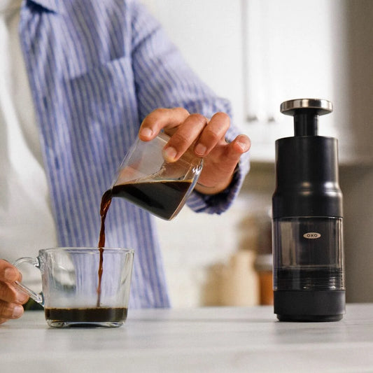 Person pouring coffee from a portafilter into a glass mug next to a coffee grinder.