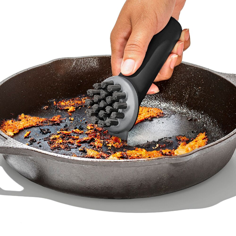 Person using a black scrubber to clean a cast iron skillet with food residue.