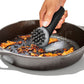 Person using a black scrubber to clean a cast iron skillet with food residue.