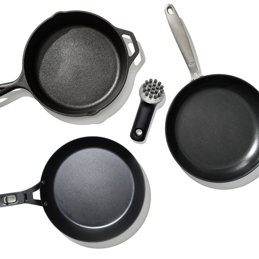 Set of black cookware including skillets and a scrubber on a white background