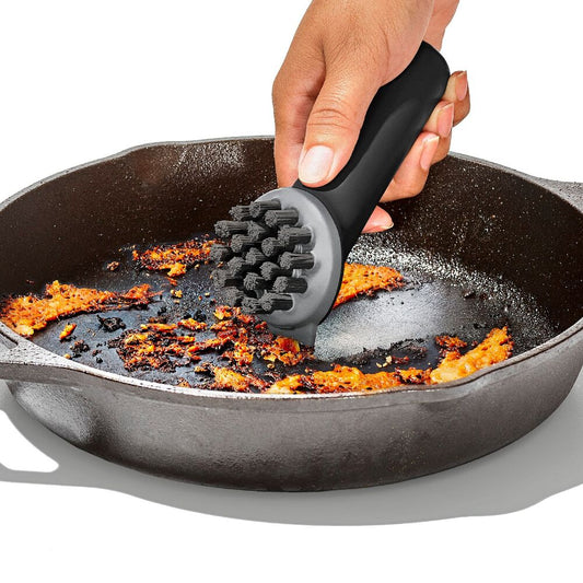 Person using a black scrubber to clean a cast iron skillet with food residue.