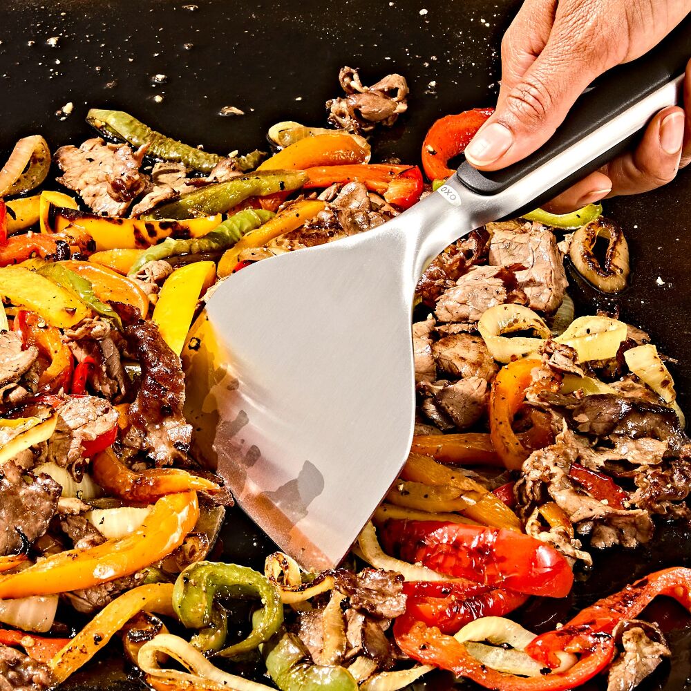 Frying pan with stir-fried vegetables and meat being stirred with a spatula.