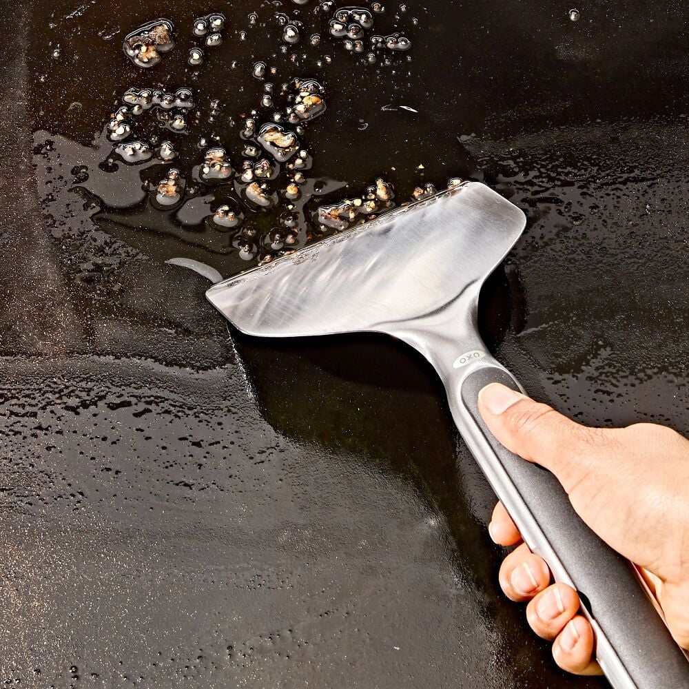 Person using a metal spatula to scrape oil from a hot surface
