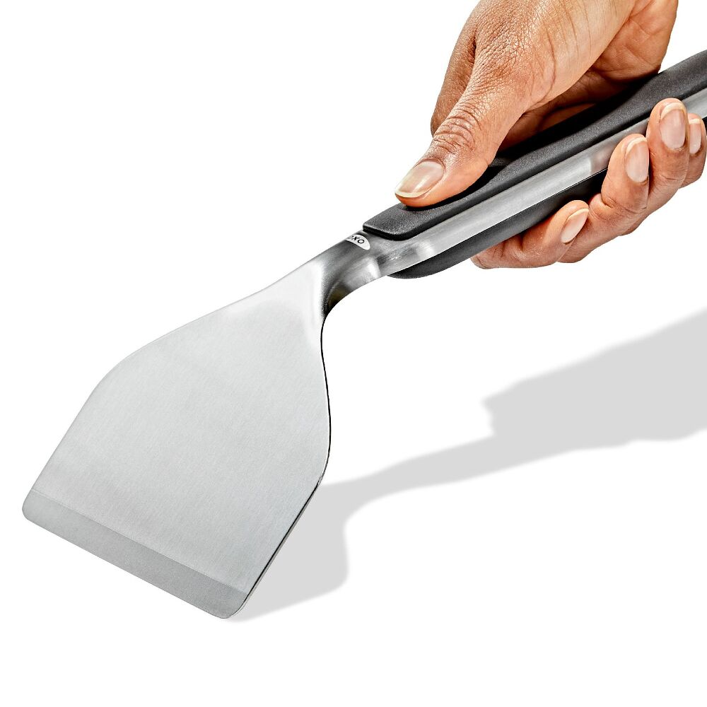 Hand holding a metal spatula with a black handle on a white background