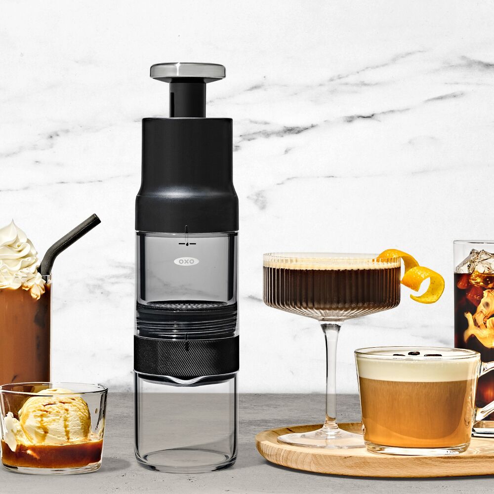 Black and clear coffee maker with various coffee beverages on a marble surface