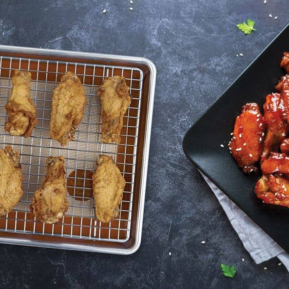 Baked chicken wings on a cooling rack and served with sauce on a black plate.
