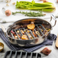 Gray silicone roaster in a stainless steel roasting pan on a table with vegetables