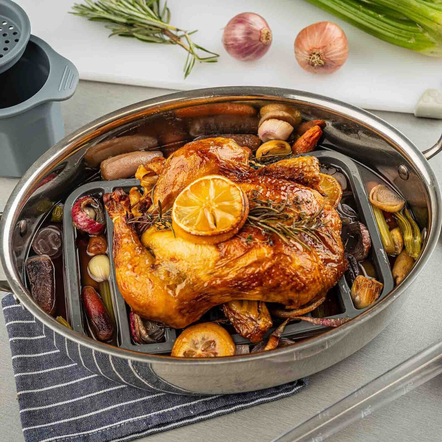 Gray silicone roaster in a stainless steel roasting pan on a table with vegetables