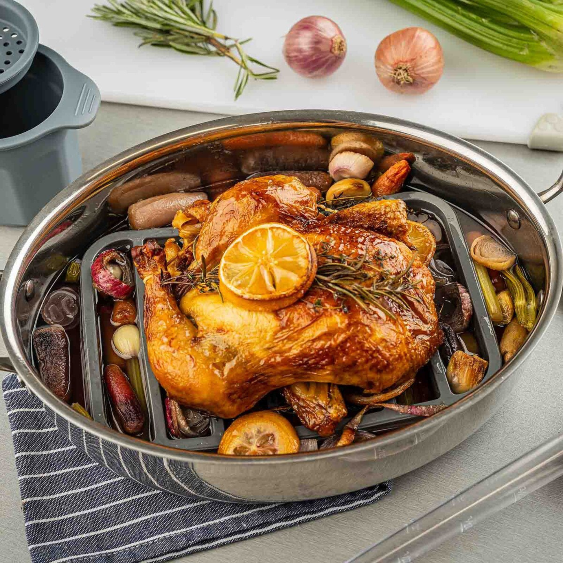 Gray silicone roaster in a stainless steel roasting pan on a table with vegetables