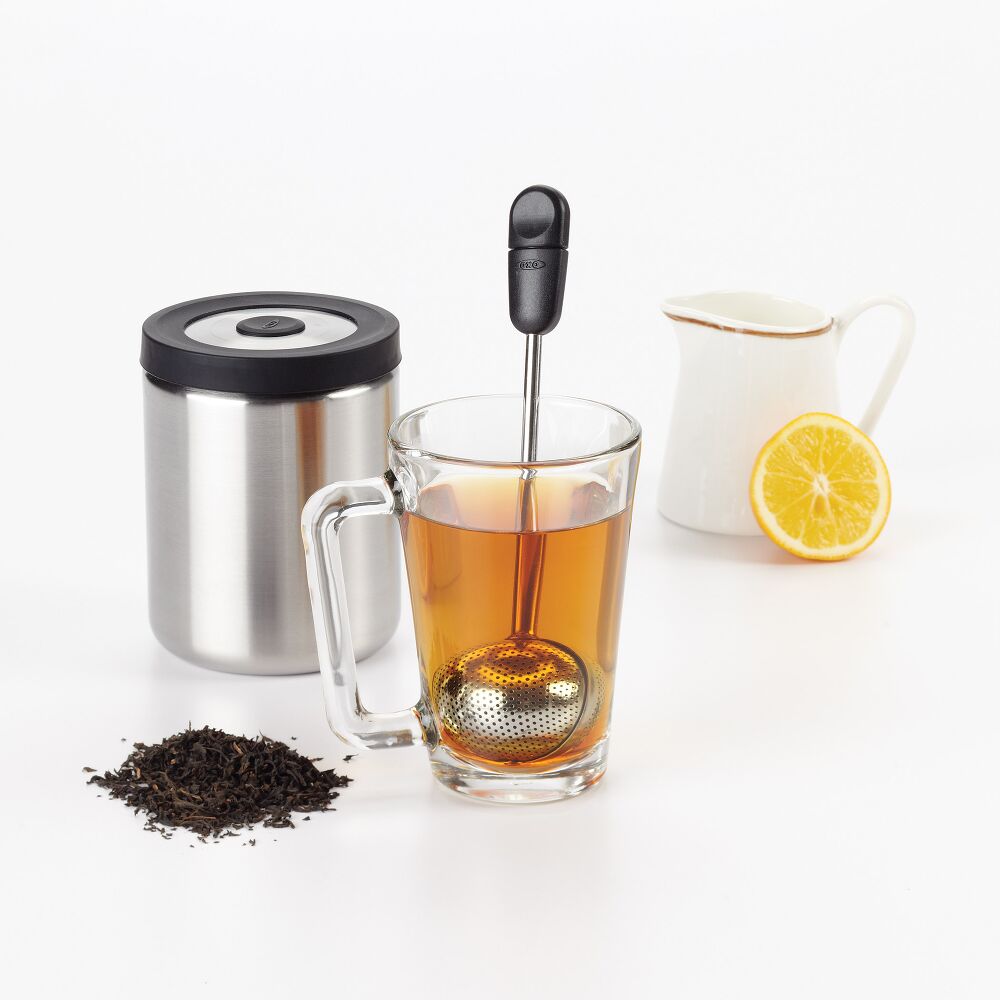 Tea-making set with glass mug, tea ball, lemon, and container on a white background